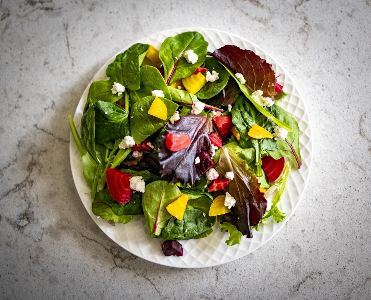 An overhead view of a plate of mixed baby greens with red and golden beet wedges and crumbled goat cheese